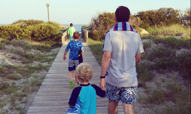 father holds young son's hand walking to the beach