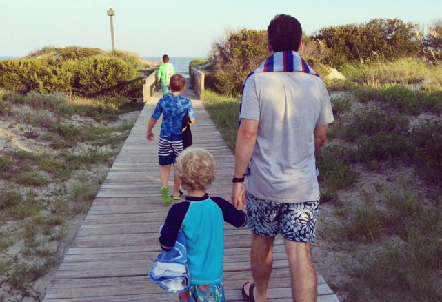 father holds young son's hand walking to the beach