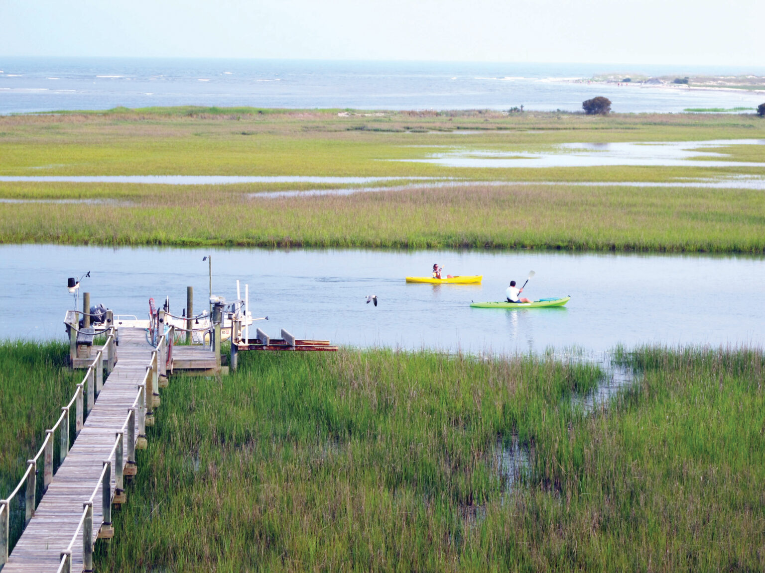 Kayakers paddle through serene tidal creeks near a private dock, showcasing the natural beauty and waterfront access offered by Seabrook Island’s gated communities.